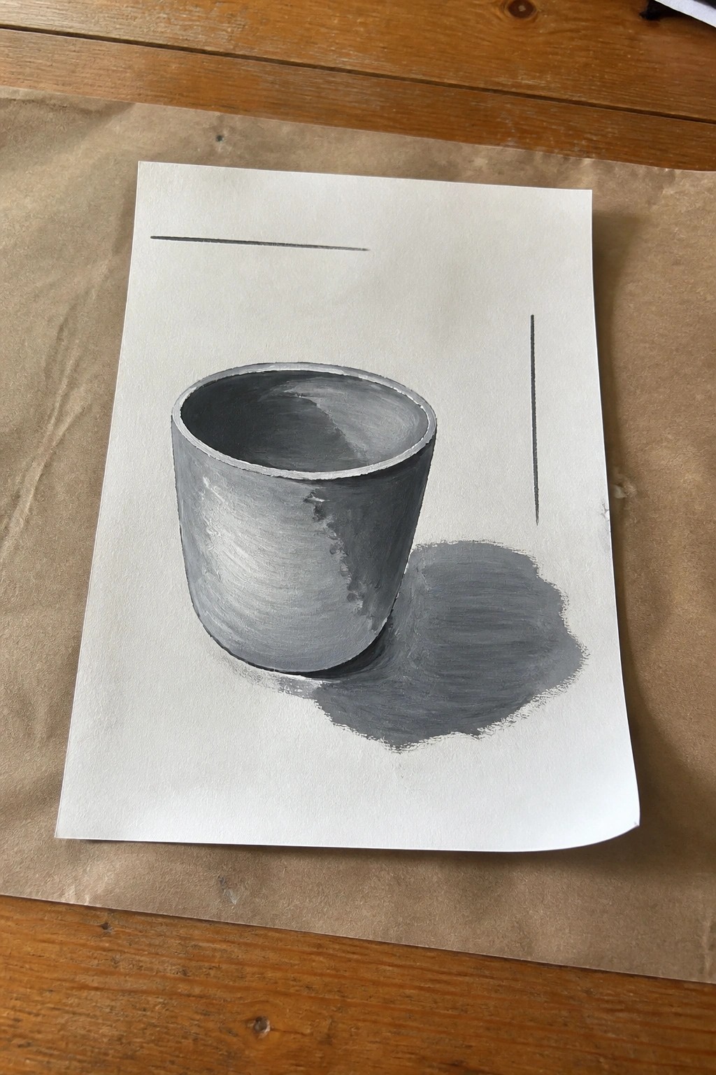 Grayscale painting of shaded cup with cast shadow on white paper over wood