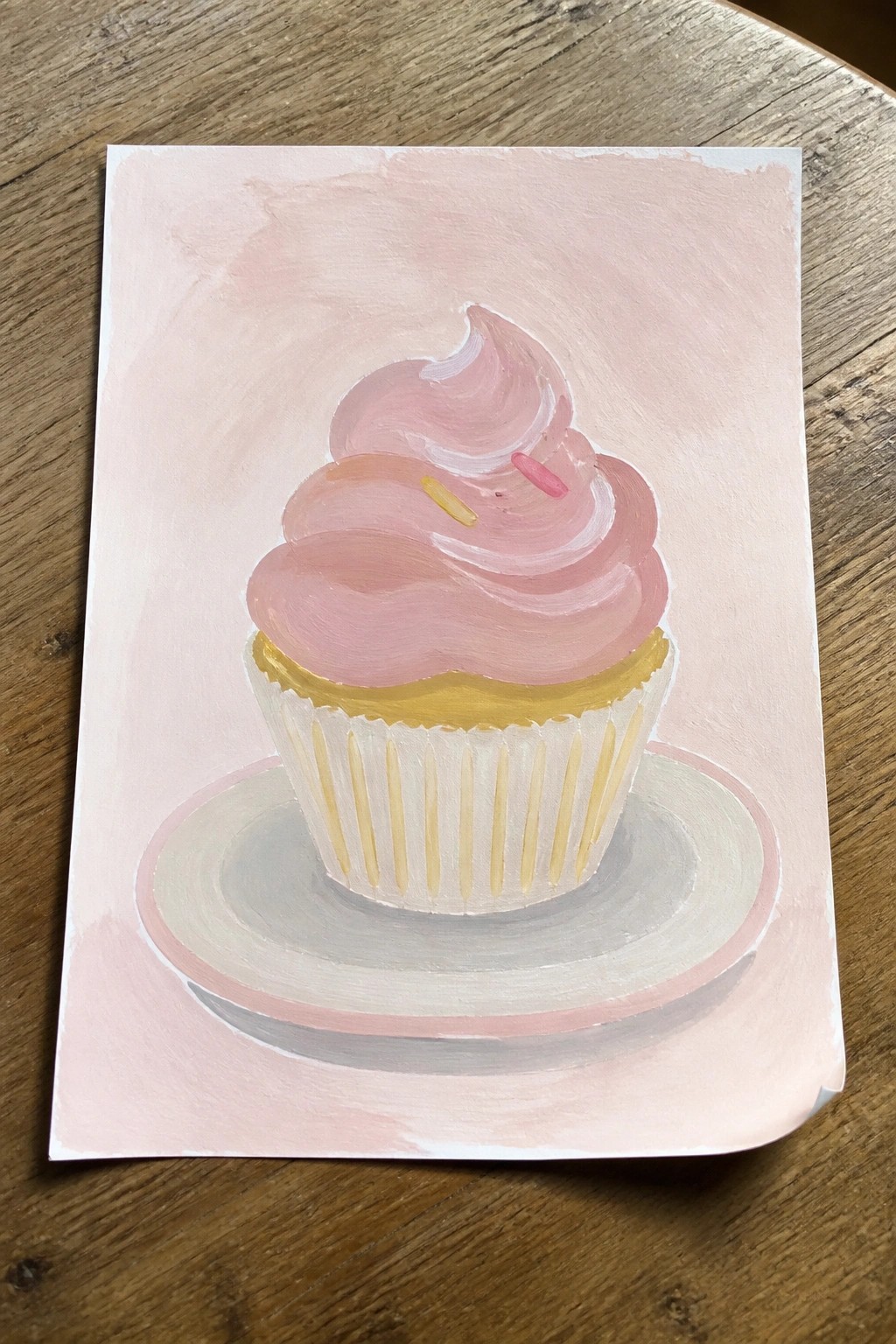 Pink-frosted cupcake painting on plate atop wooden surface