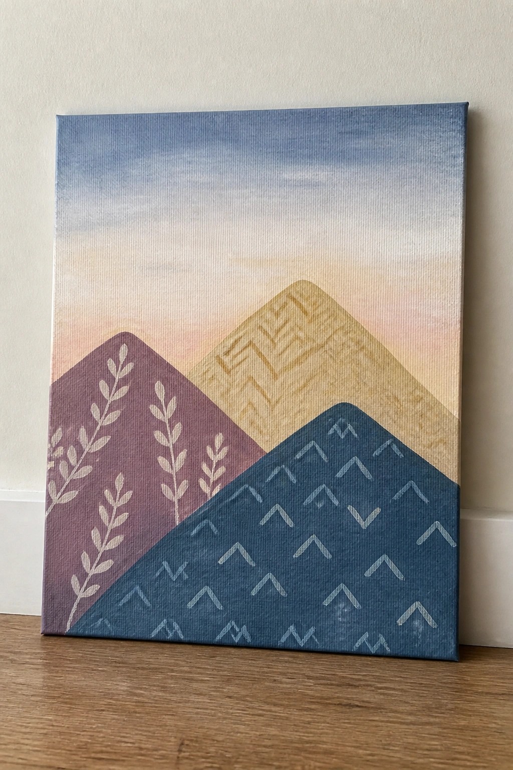 Abstract canvas painting of patterned mountains in purple, gold, and blue under pastel sky