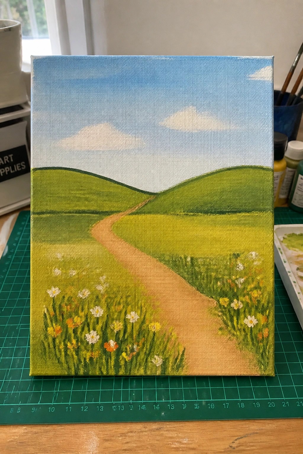 Vibrant landscape painting of winding path through green hills and wildflower meadow under blue sky