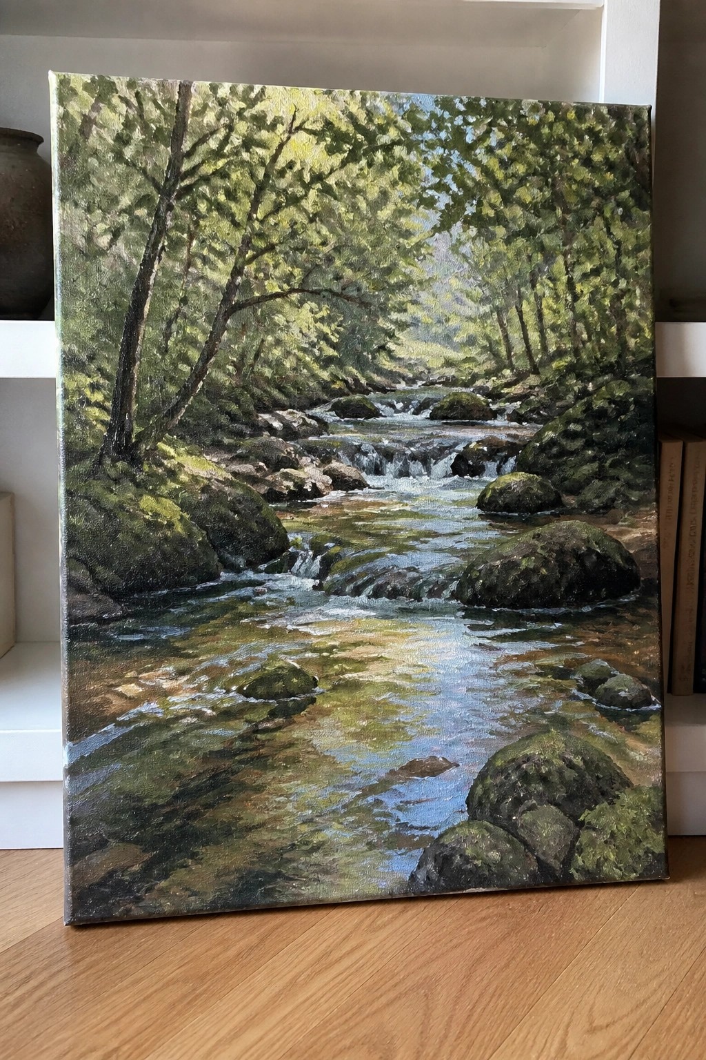 Realistic oil painting of a rocky forest stream with moss-covered boulders and leafy trees.