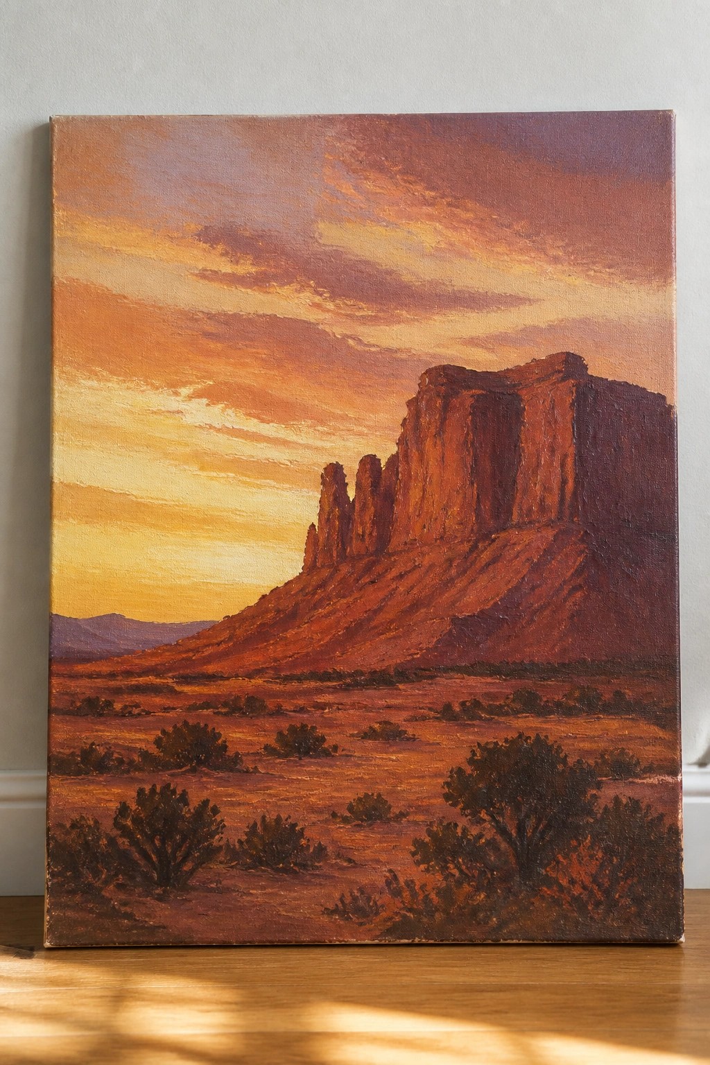 An oil painting of a desert landscape at sunset with large red rock mesas, scattered shrubs, and a colorful sky.