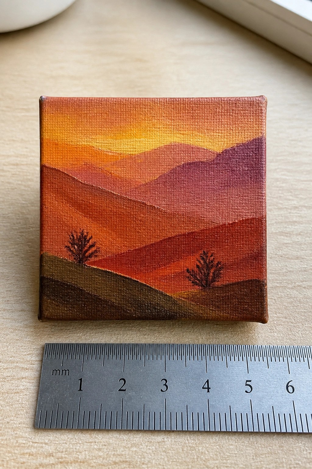 Tiny canvas shows layered orange sunset mountains with two trees beside ruler
