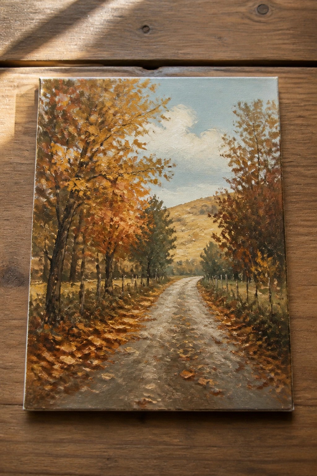 Autumn oil painting of winding dirt road amid colorful trees on wood table