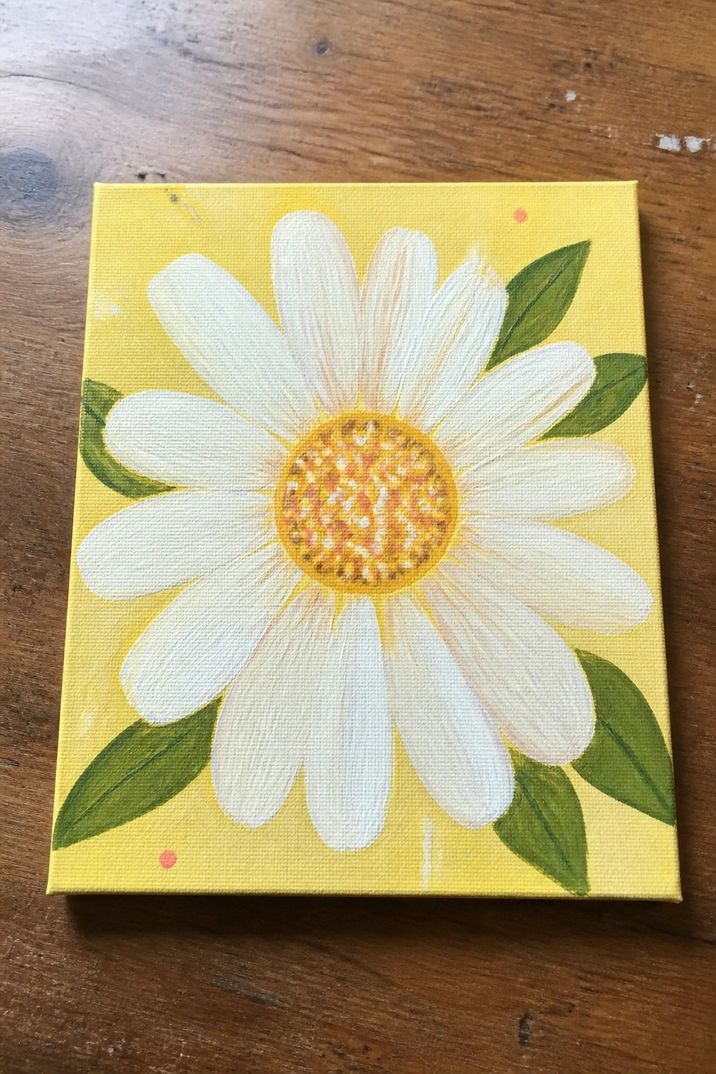 Yellow canvas with white daisy, orange center, and green leaves on wood