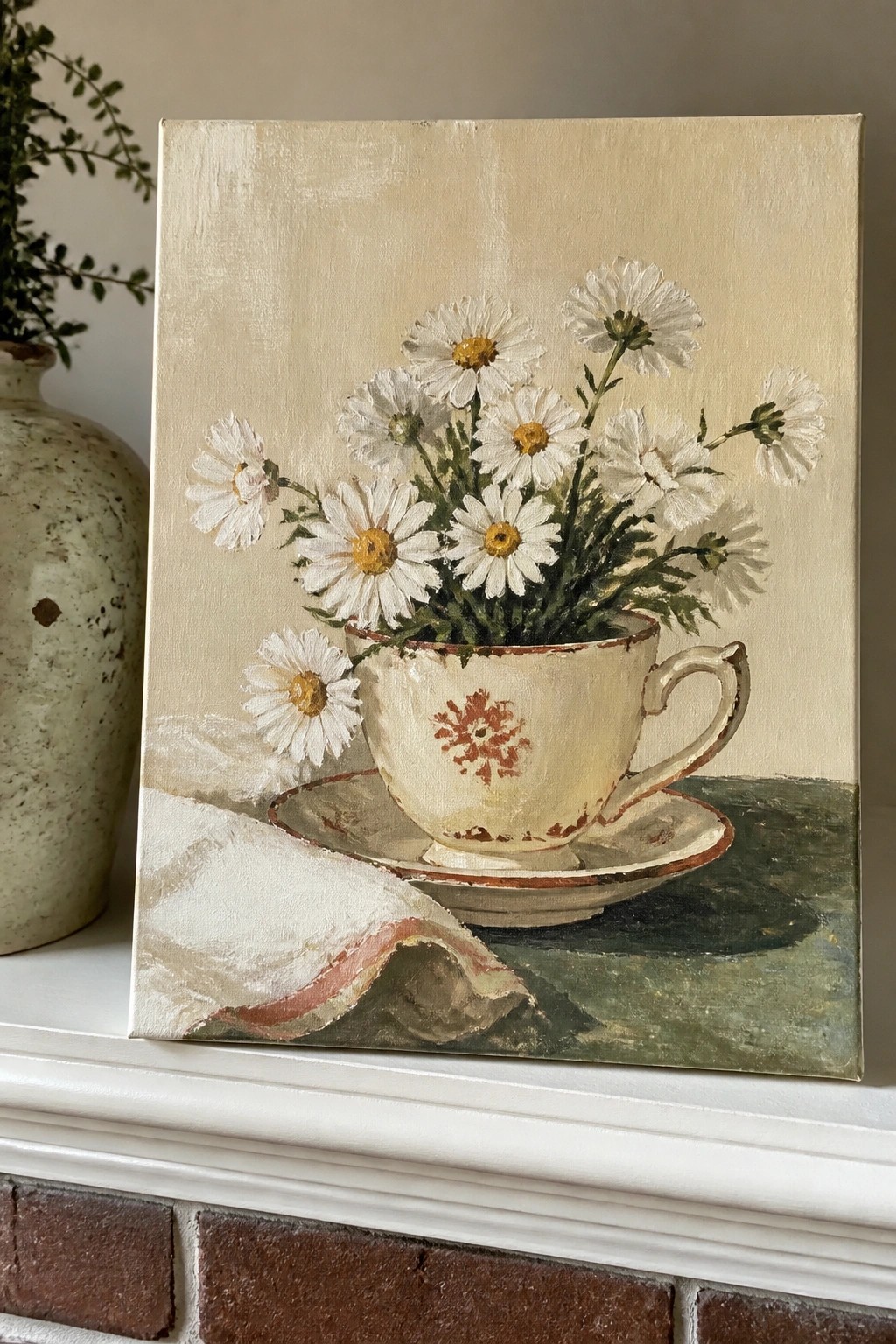 A painting of white daisies arranged in a white teacup with red patterns, resting on a saucer with a draped cloth nearby.