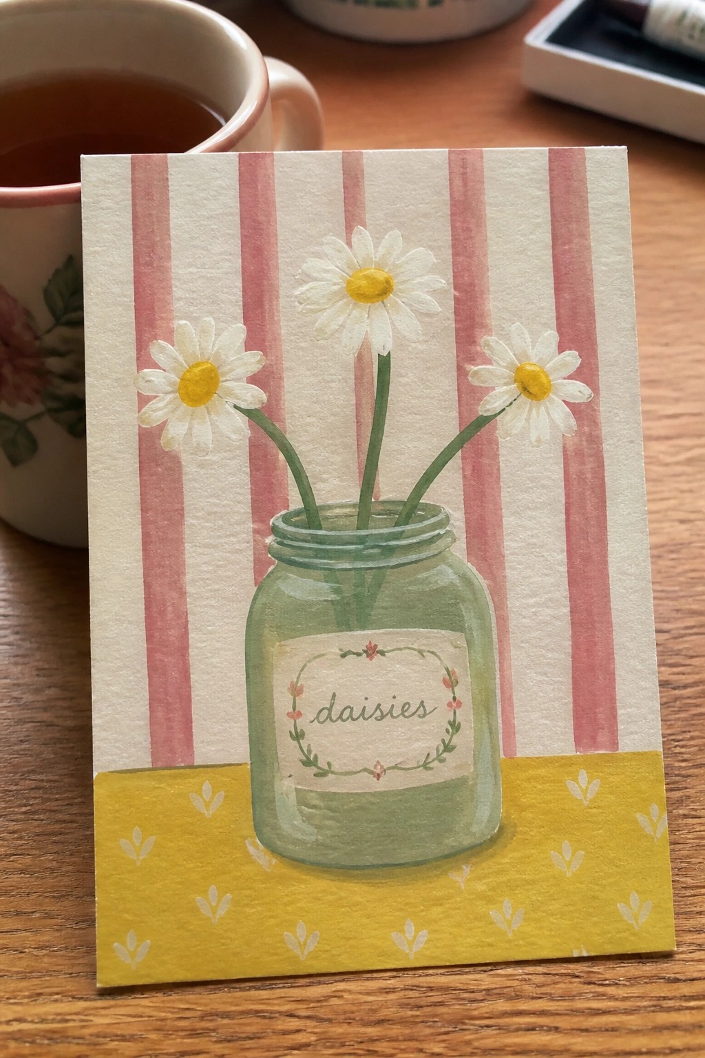 A watercolor painting of three white daisies in a green mason jar labeled
