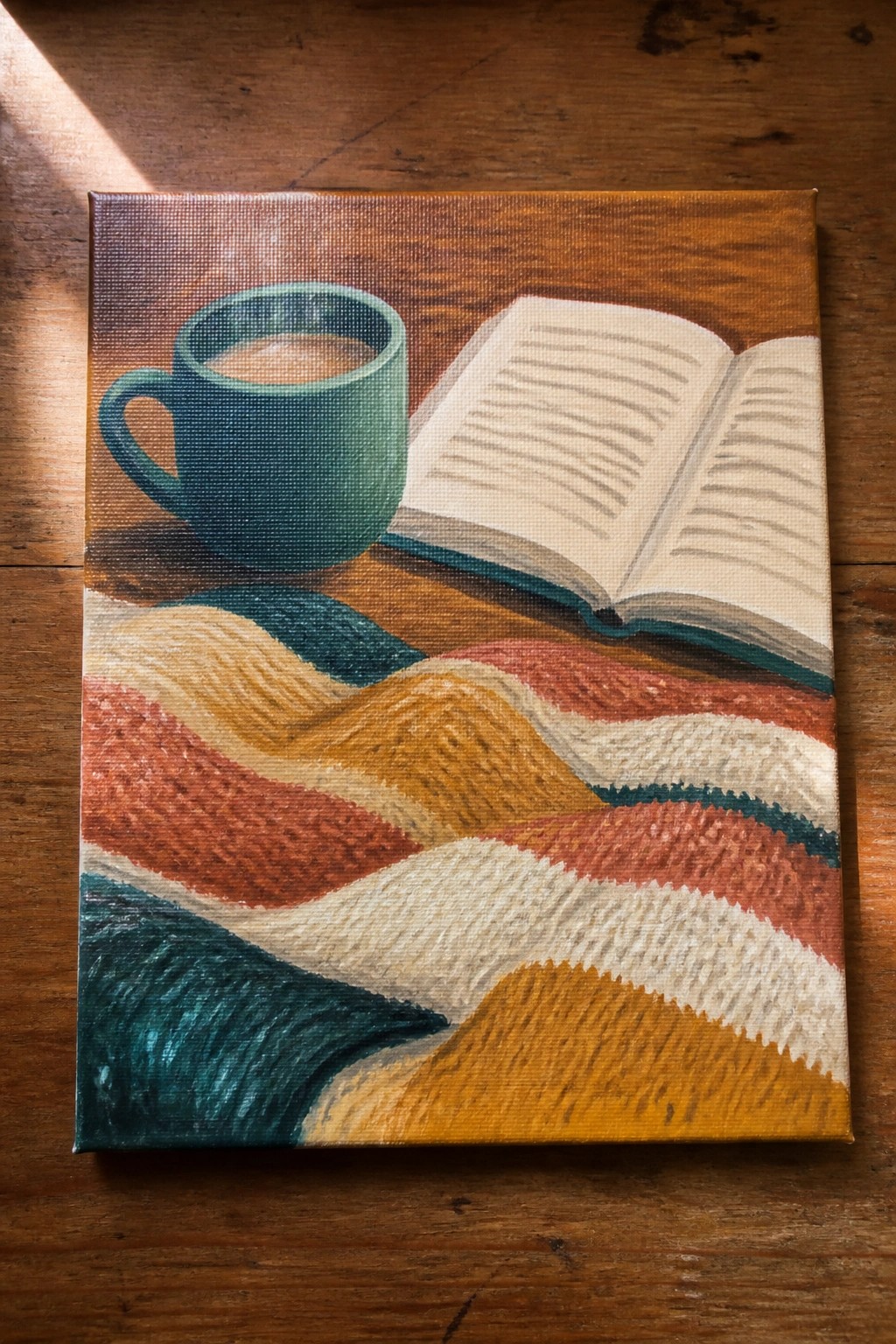 Painting of steaming teal mug and open book on colorful wavy striped blanket