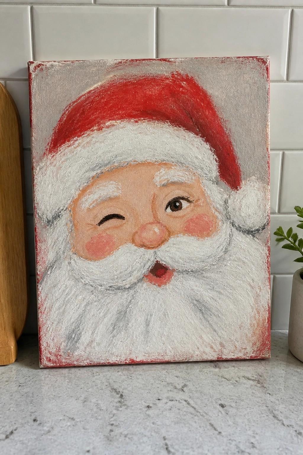 Winking Santa Claus painting on canvas with red hat and white beard on counter