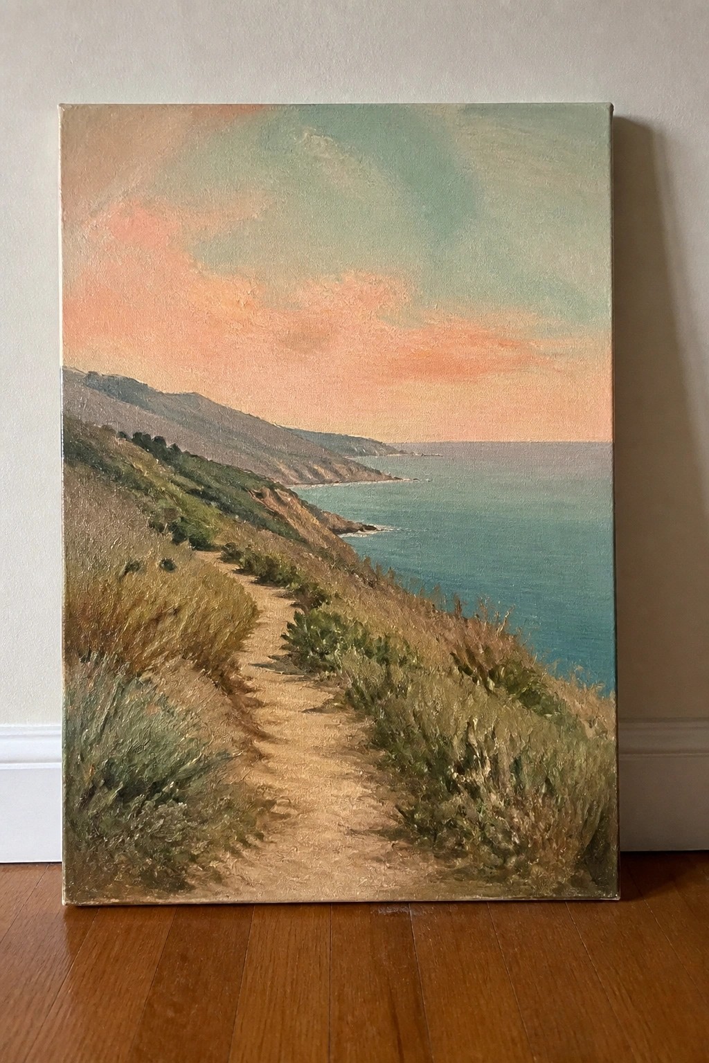 Coastal hillside path winds toward turquoise sea beneath vibrant pink-green sunset sky.