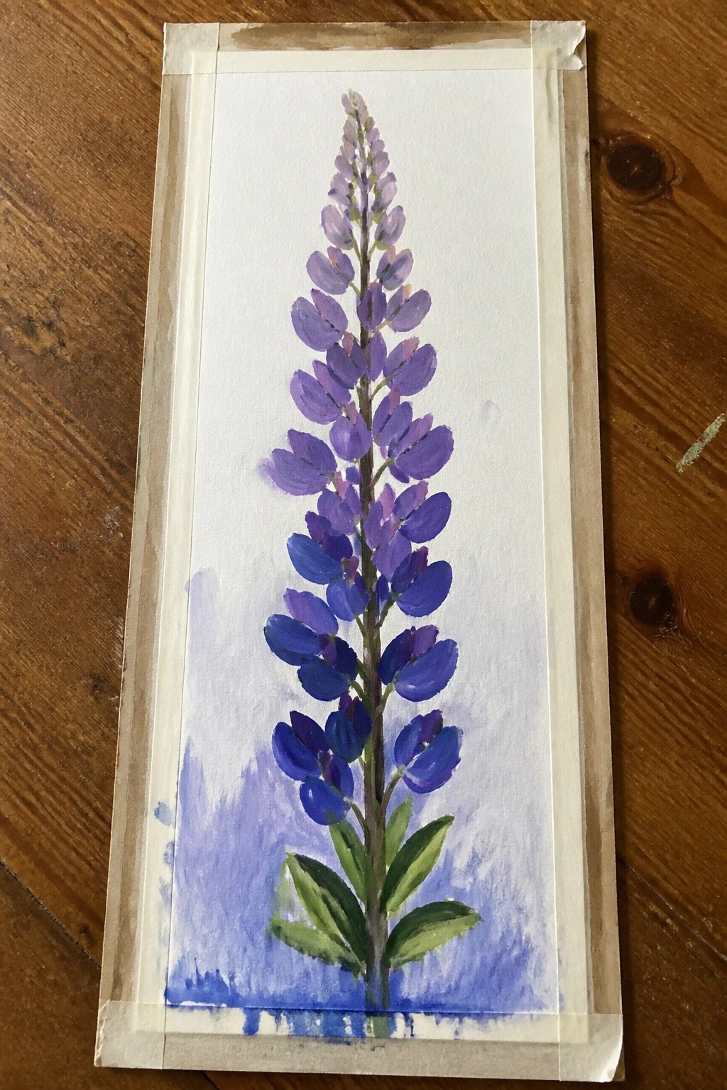 A vertical painting of a tall purple lupine flower with green leaves on white paper taped to wood.