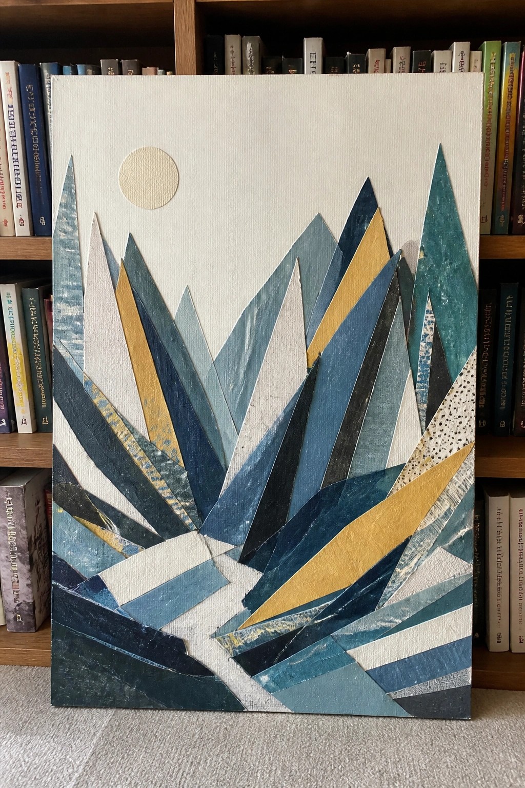 Abstract geometric collage of angular blue mountains with gold accents and pale sun before bookshelves.