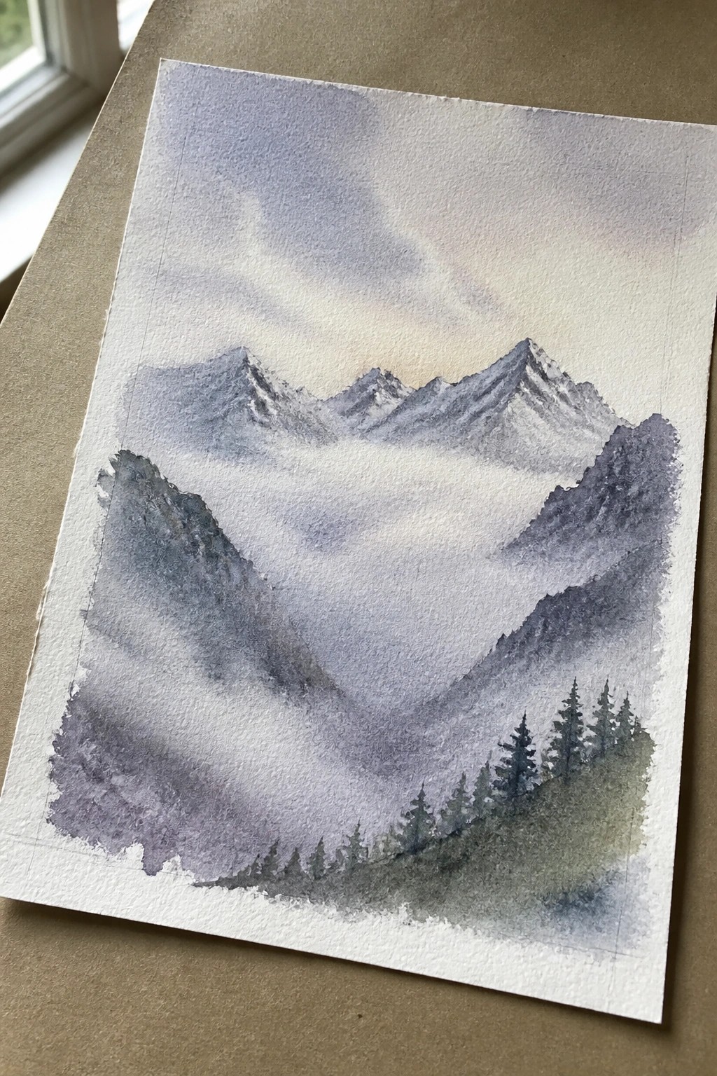 Watercolor of misty purple mountains with snow peaks and foreground pine trees
