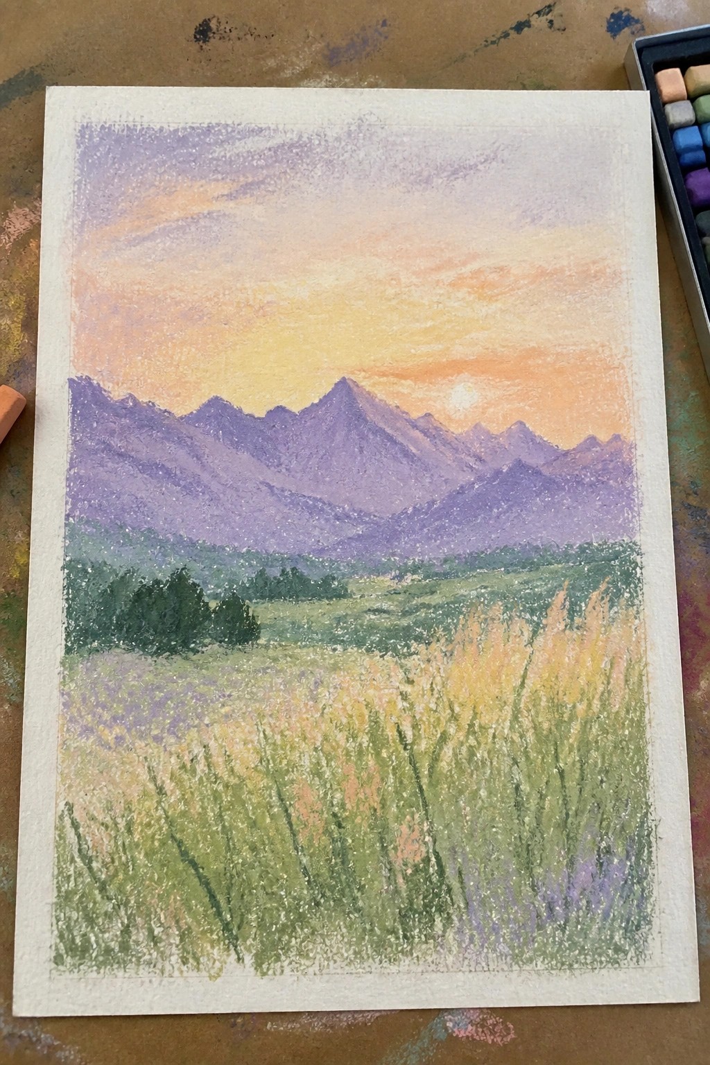 Pastel landscape of purple mountains at sunset over a golden-green wildflower meadow
