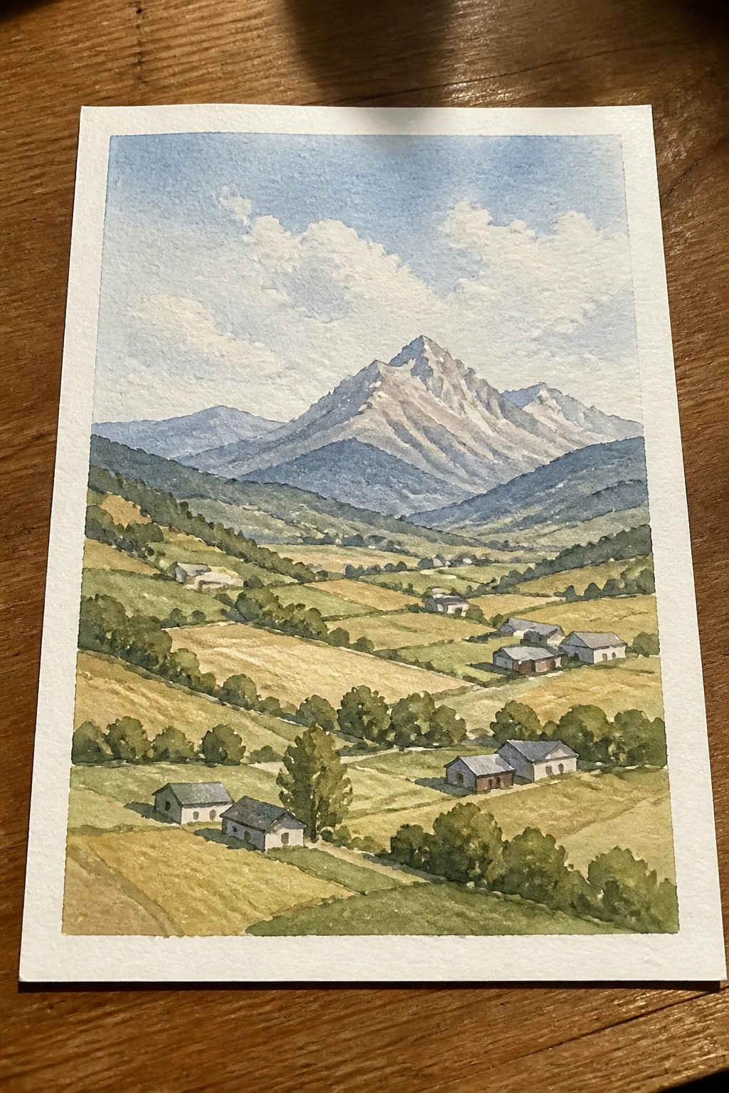 Watercolor landscape of rolling fields, scattered houses, and a snow-capped mountain peak.