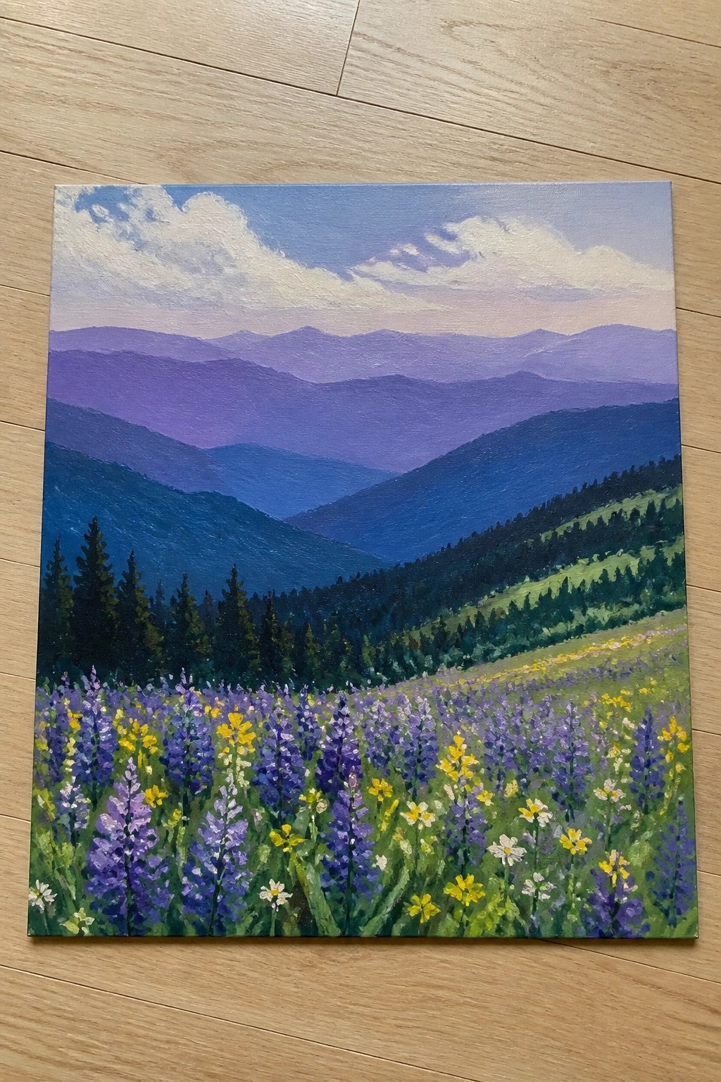 Layered purple mountains rise above a vibrant meadow of purple, yellow, and white wildflowers.