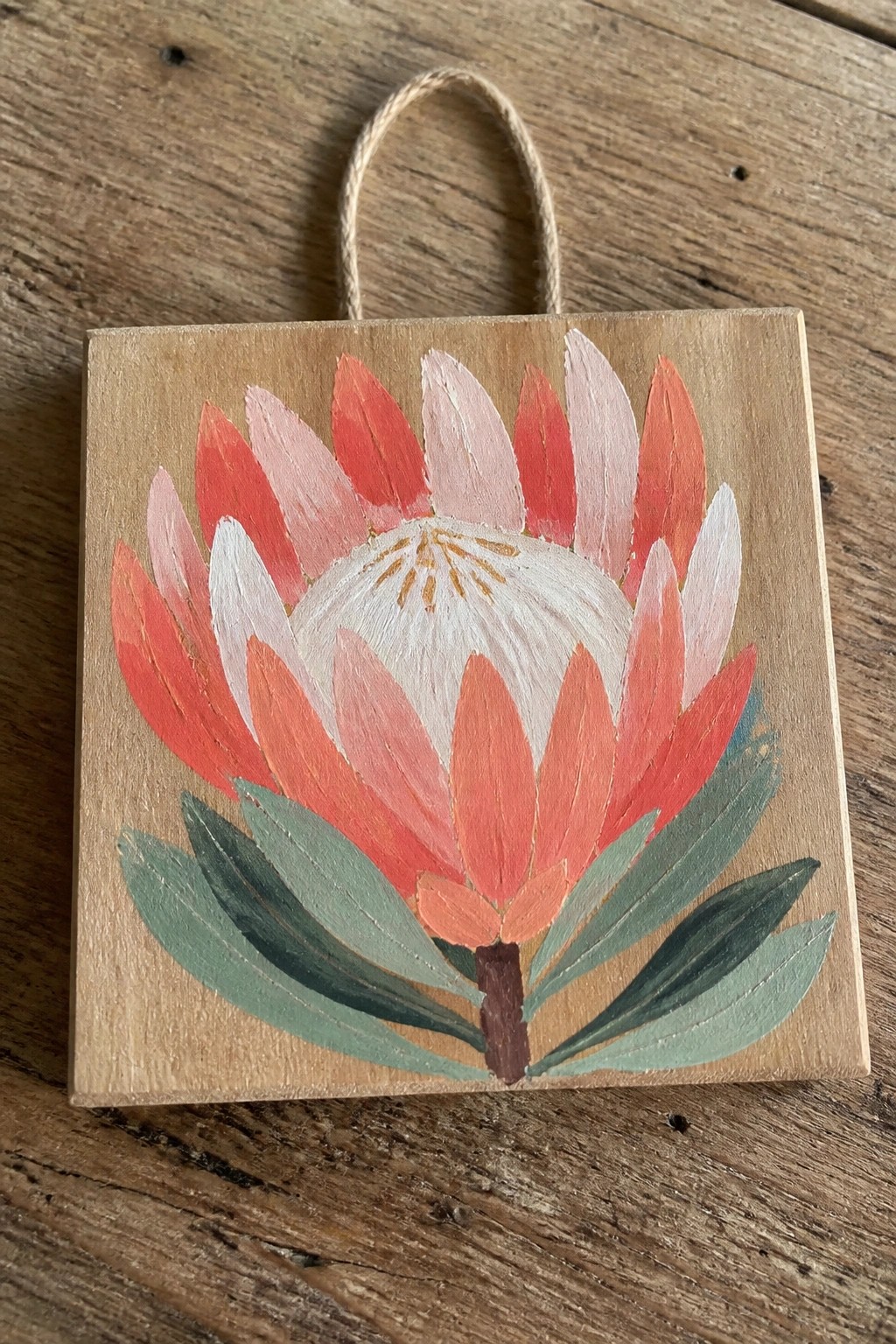 Hand-painted red-pink protea flower on square wooden plaque with twine loop