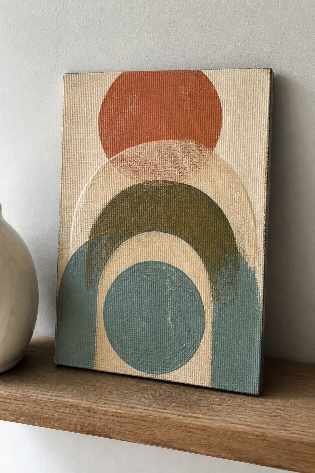 Abstract painting with overlapping circles in orange, green, and teal on wooden shelf