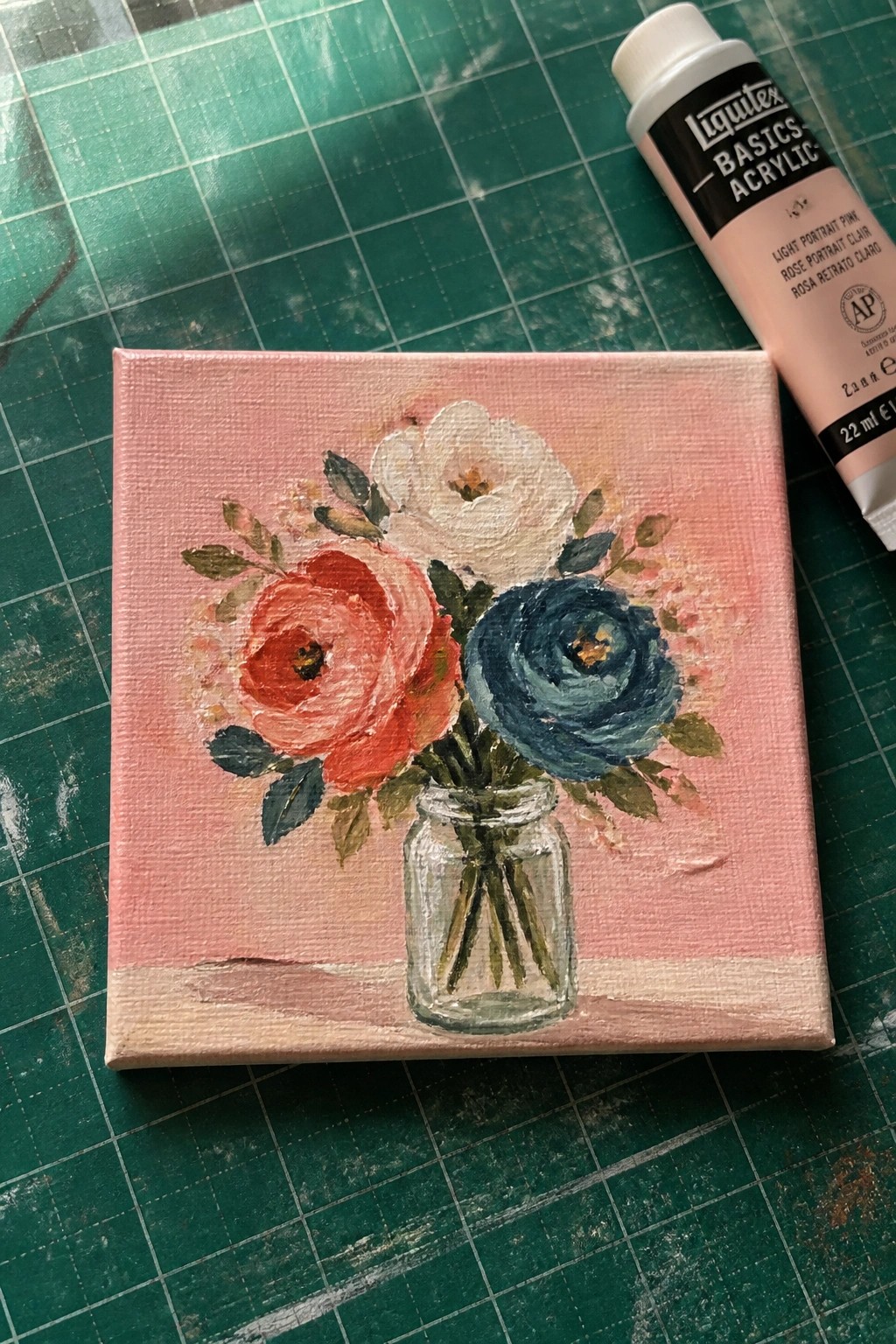 Pink canvas floral painting of flowers in glass jar beside pink acrylic paint tube