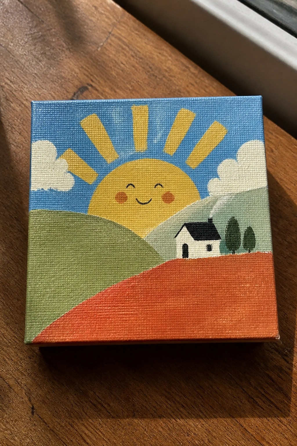 Cute painting of smiling sun above white house on green and orange hills