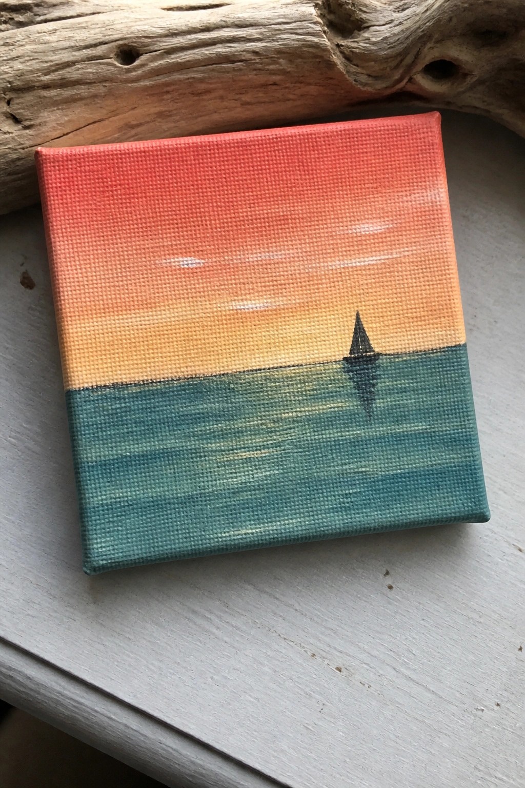 Small square canvas painting of sailboat on teal sea under red-orange sunset sky.
