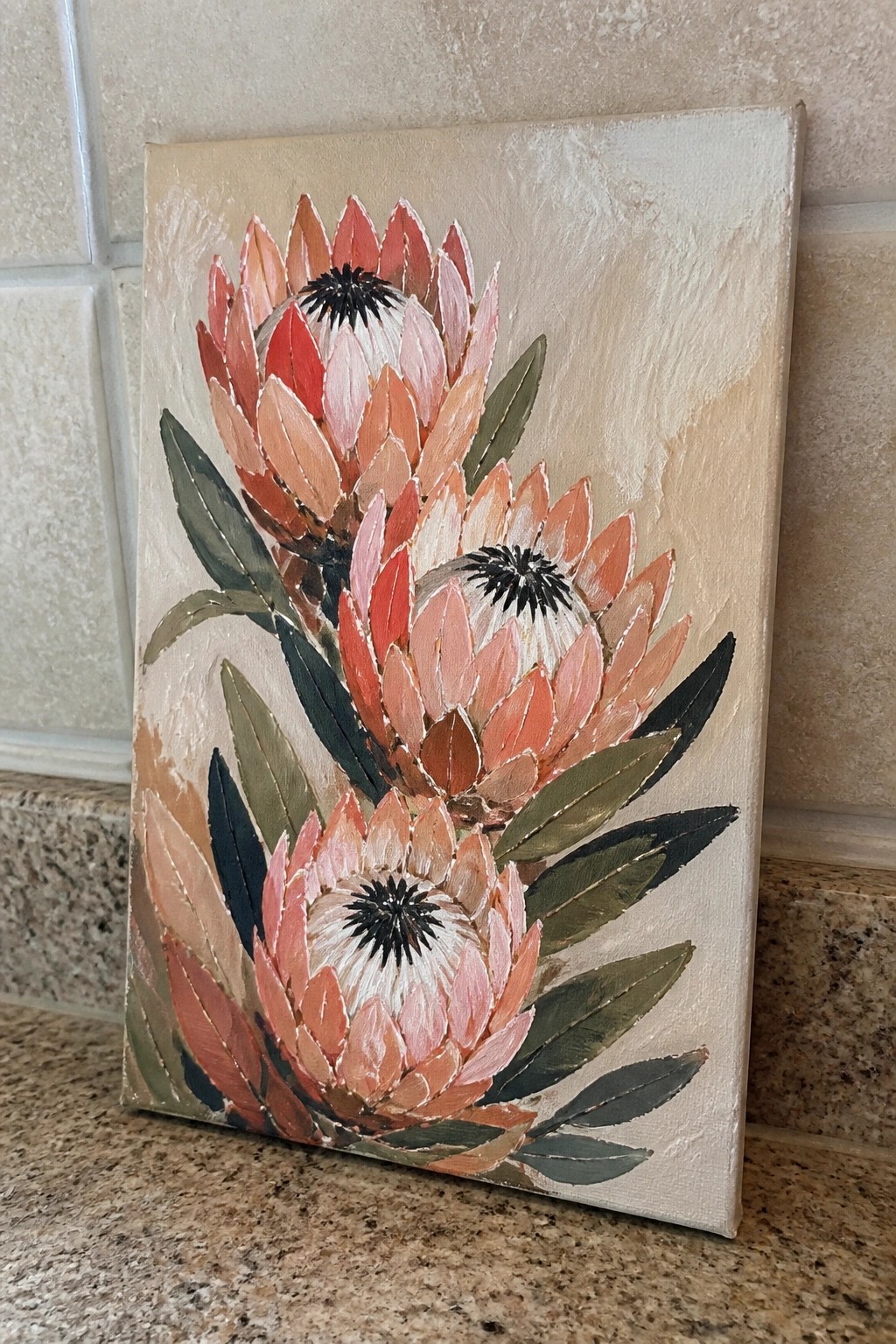 Three pink protea flowers with dark centers and green leaves on beige canvas.