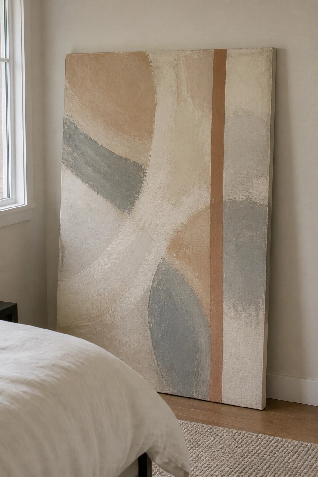 Large abstract painting with neutral beige and gray curves leaning against bedroom wall