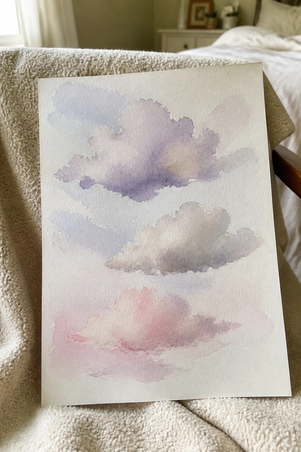 Soft purple and pink watercolor clouds on paper resting on a white fluffy blanket.