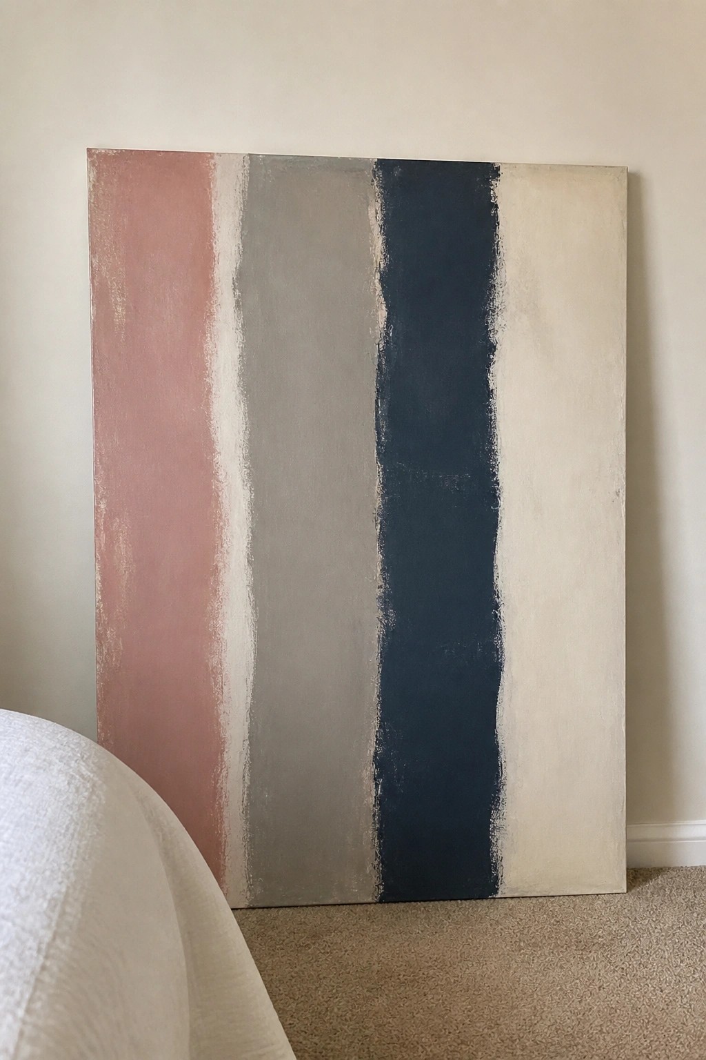 Abstract painting with vertical pink, gray, navy, and beige stripes leaning on wall