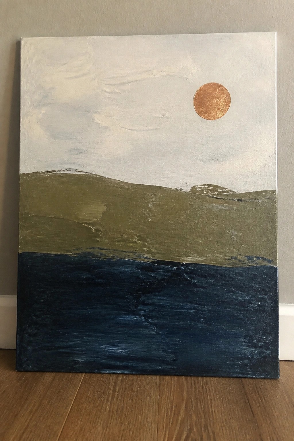 Abstract landscape with copper sun in pale sky above green hills and dark blue water.