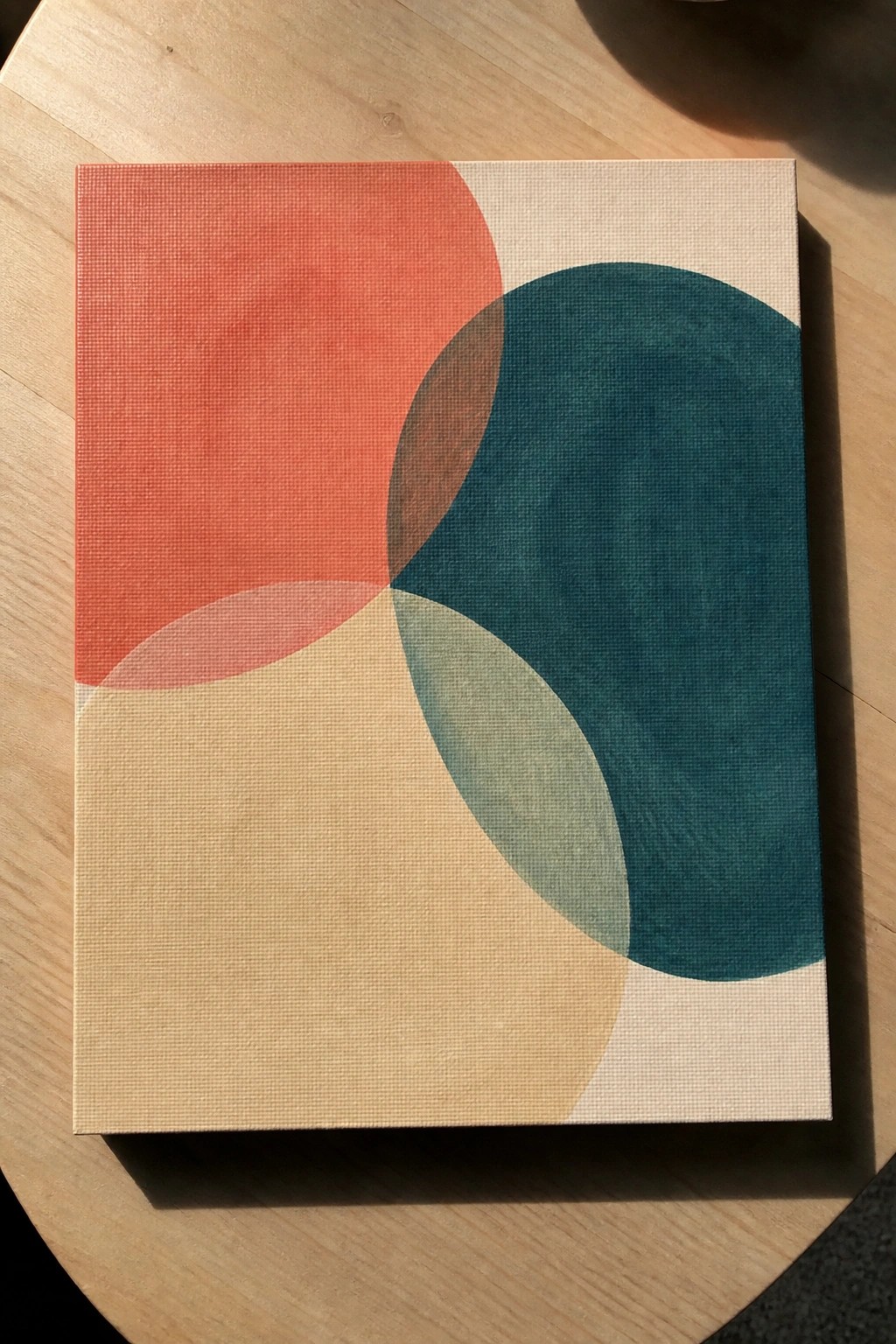 Abstract canvas with overlapping coral, teal, and beige circles on wooden surface.