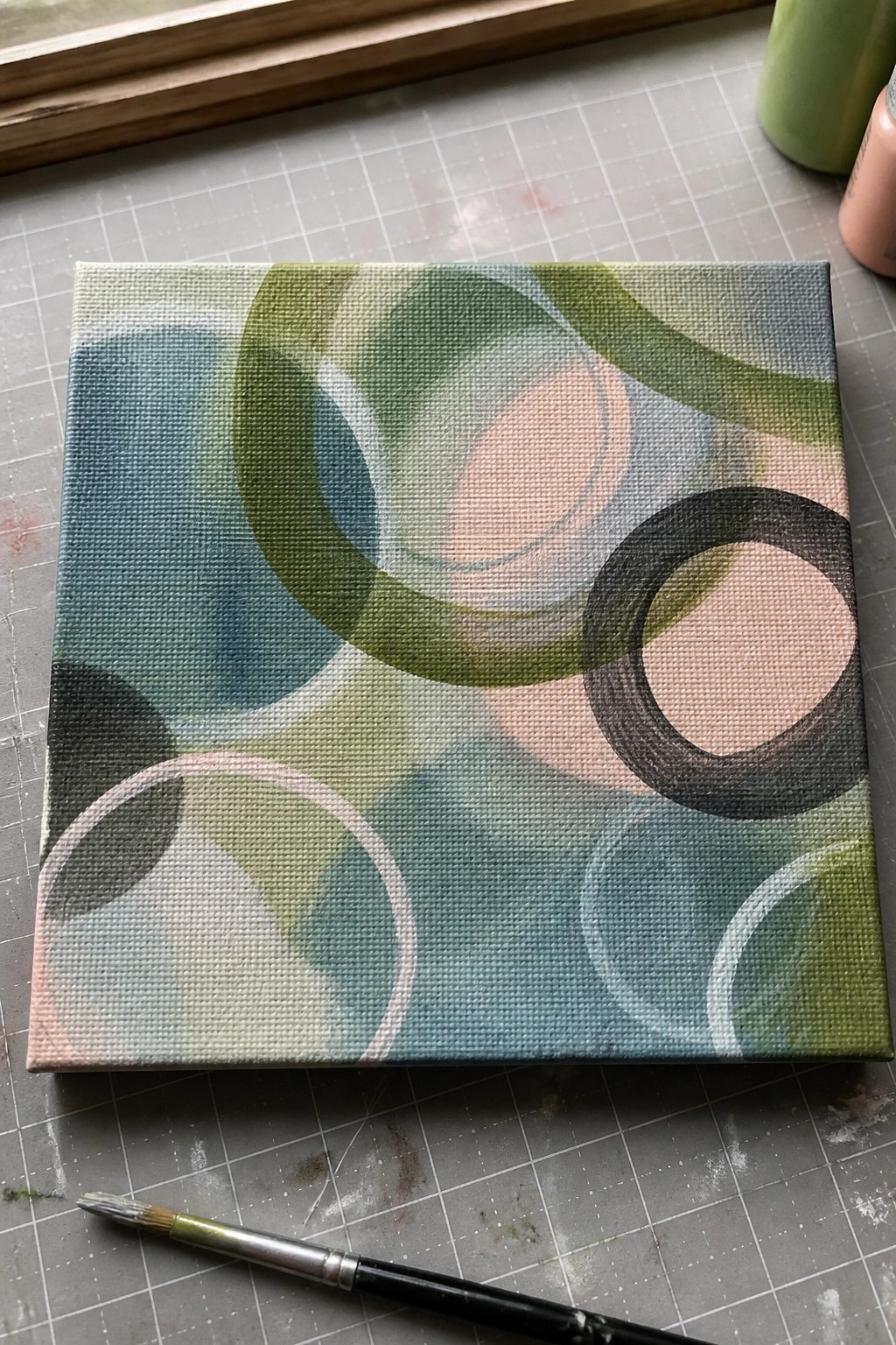 Abstract canvas with overlapping green, blue, and pink circles beside paintbrush on mat