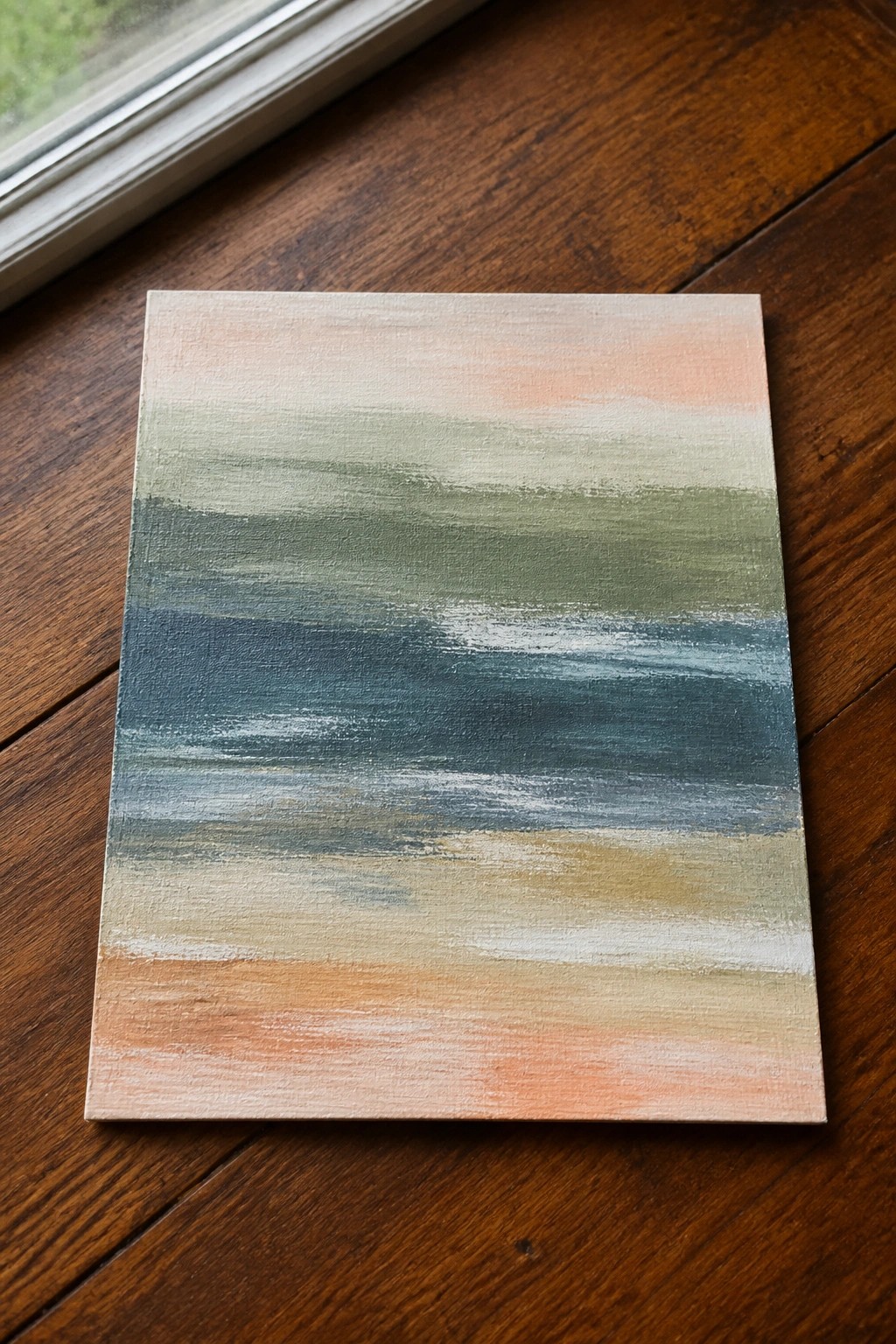 Abstract painting with soft horizontal brushstrokes in peach, green, blue, and beige on wood floor