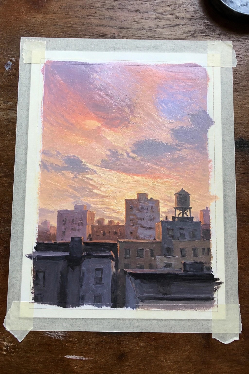 Cityscape painting of rooftops and water tower beneath vibrant pink-orange sunset sky