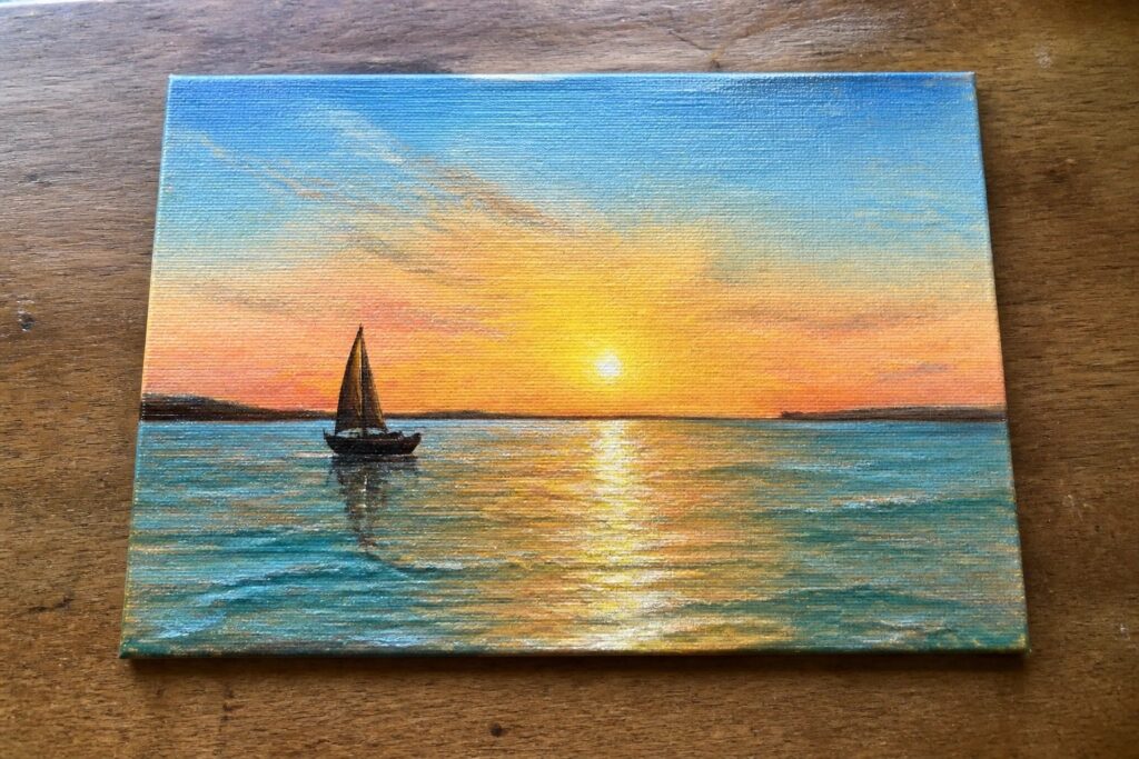 Sailboat on calm sea beneath vibrant orange sunset sky with golden reflections.