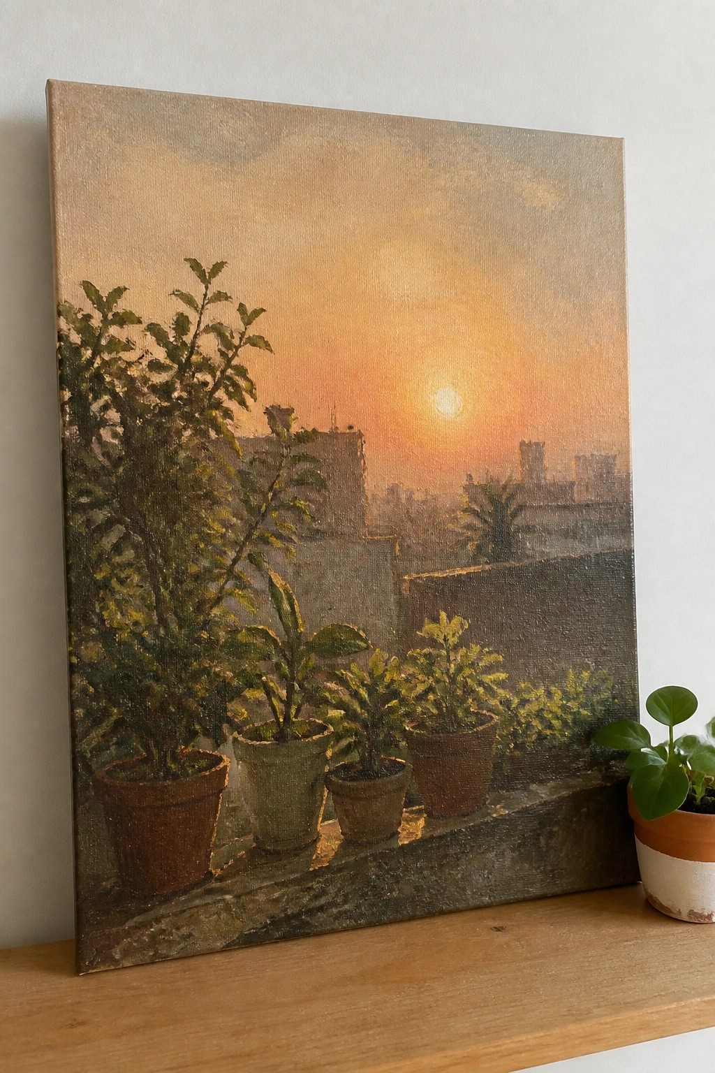 Painting of potted plants overlooking city sunset on wooden shelf with real plant