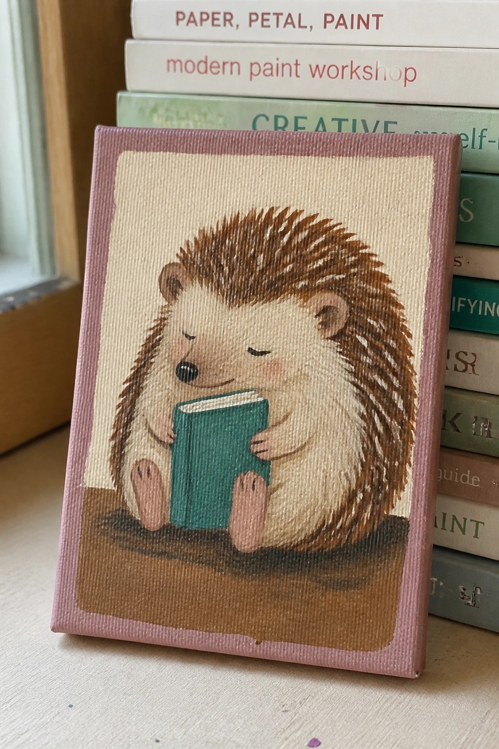 Cute hedgehog clutching green book on pink-bordered canvas, books behind