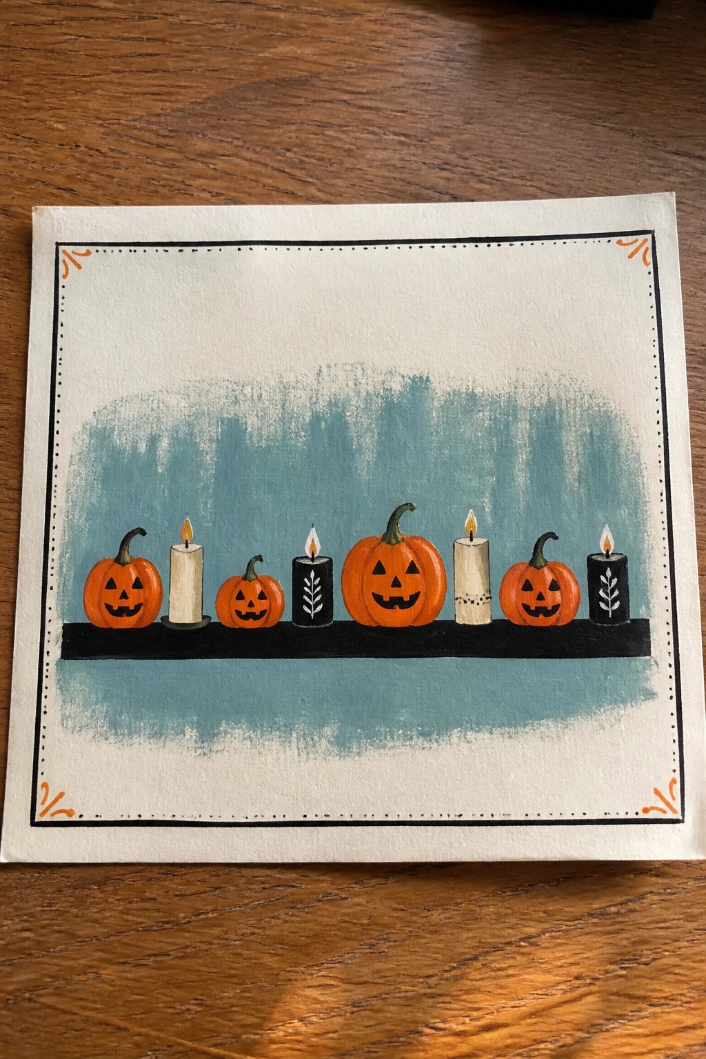 Watercolor painting of jack-o'-lanterns and lit candles lined on a black shelf with teal background