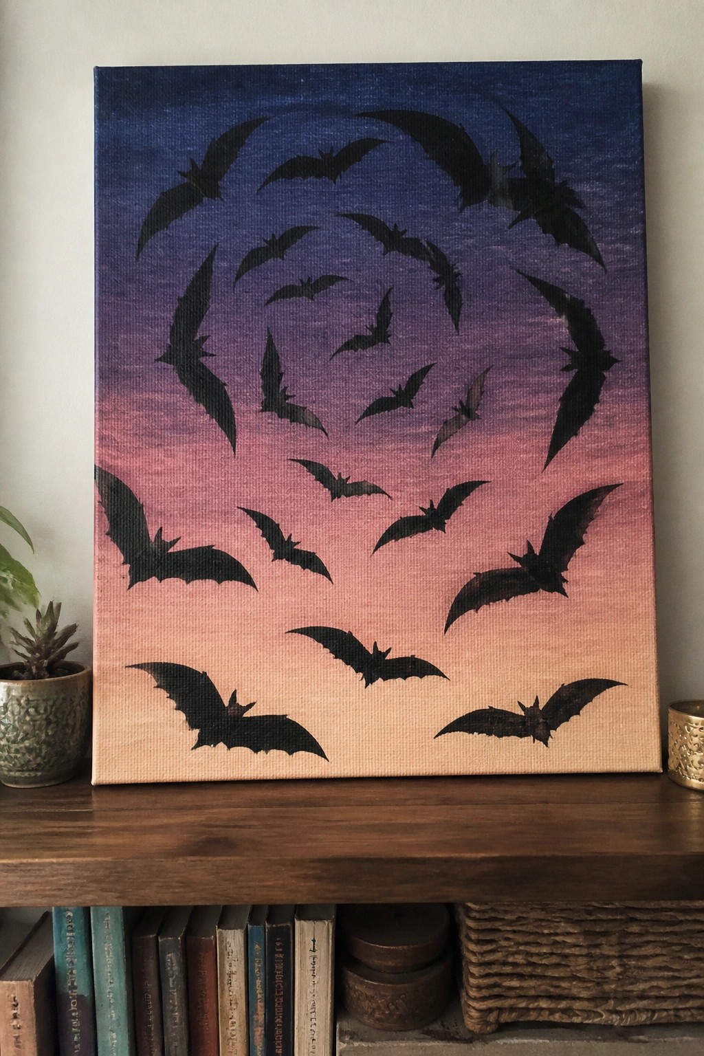 Black bat silhouettes swirl across a blue-purple-pink gradient canvas on a shelf.