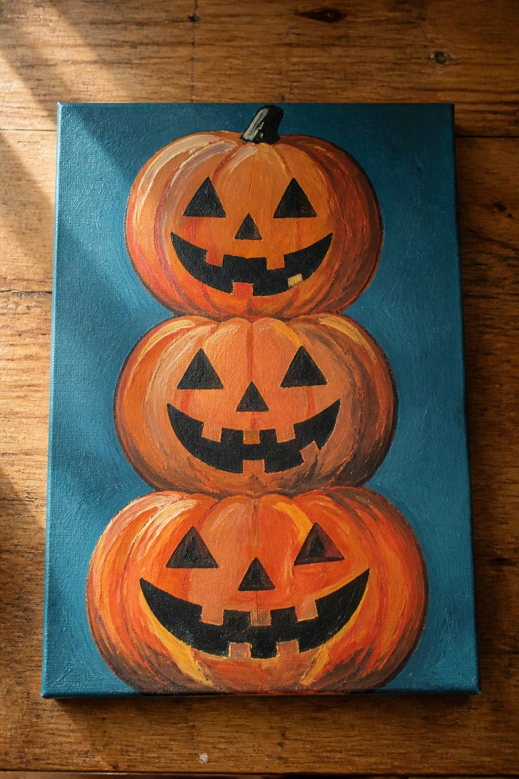 Three stacked orange jack-o'-lanterns with carved faces on teal canvas.