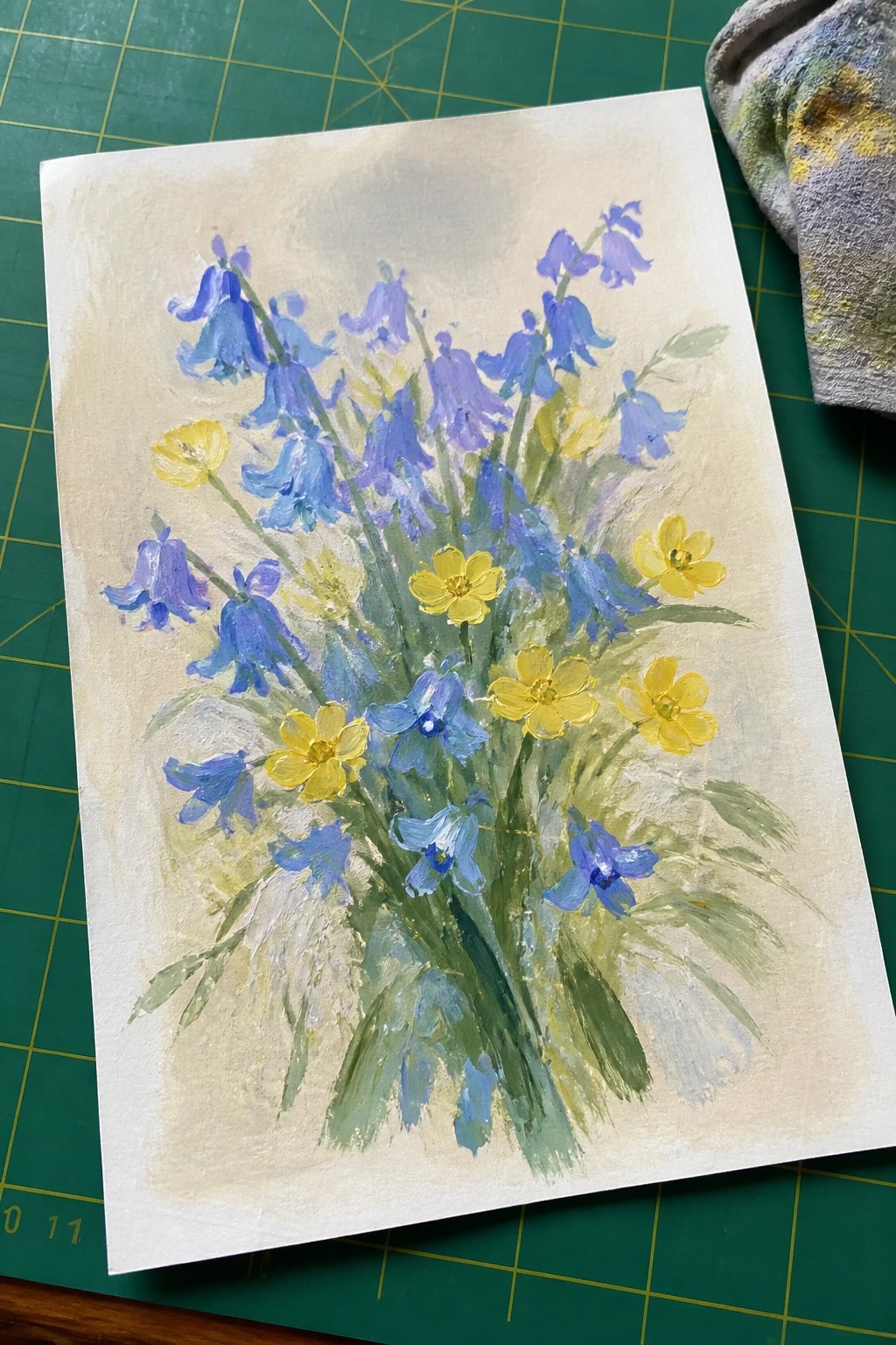 Loose painting of blue bluebells and yellow flowers on green cutting mat