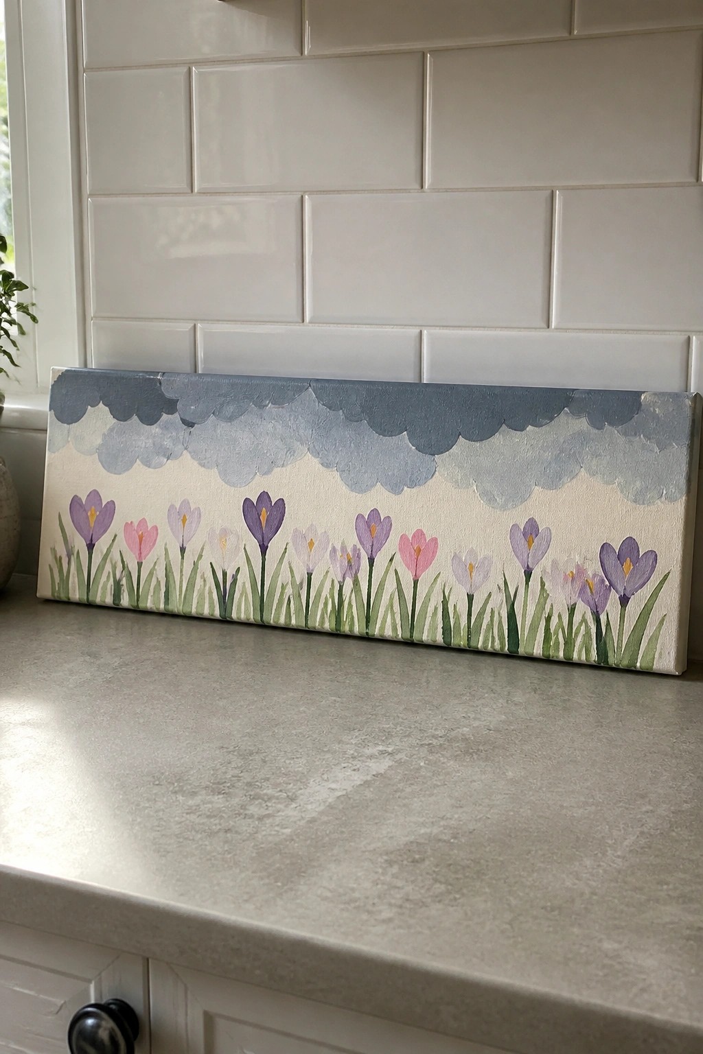Canvas painting of pink and purple crocuses under blue clouds on kitchen counter