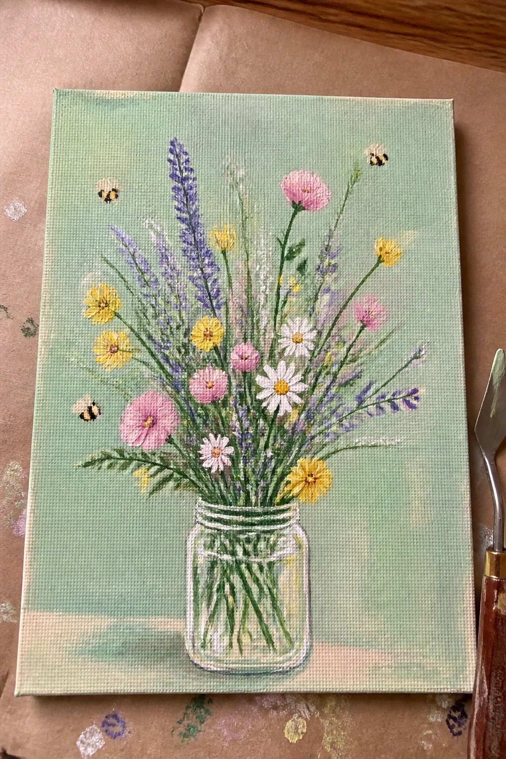 Colorful wildflowers in glass mason jar with bees on light green canvas background