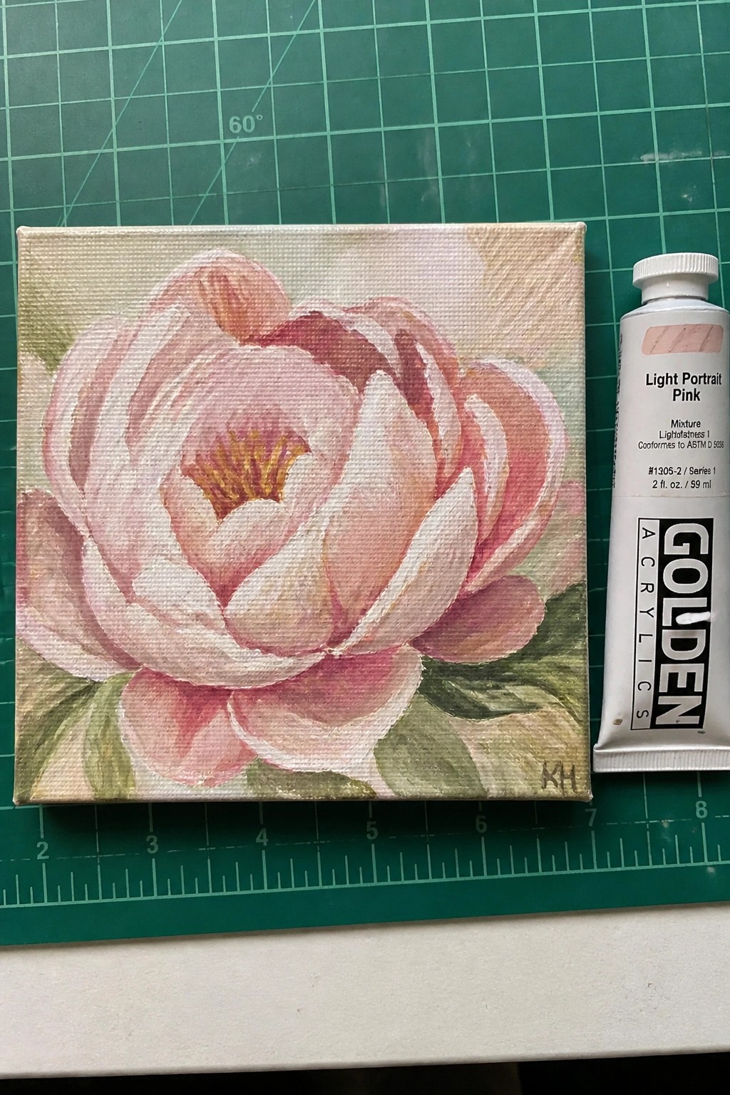 Canvas painting of pink peony flower beside tube of light portrait pink acrylic paint.
