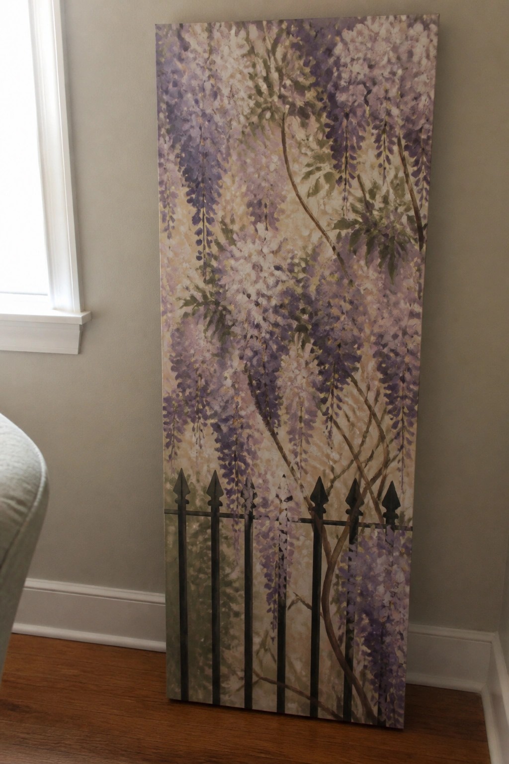 A tall acrylic painting shows purple and white wisteria flowers hanging down over a black metal fence.