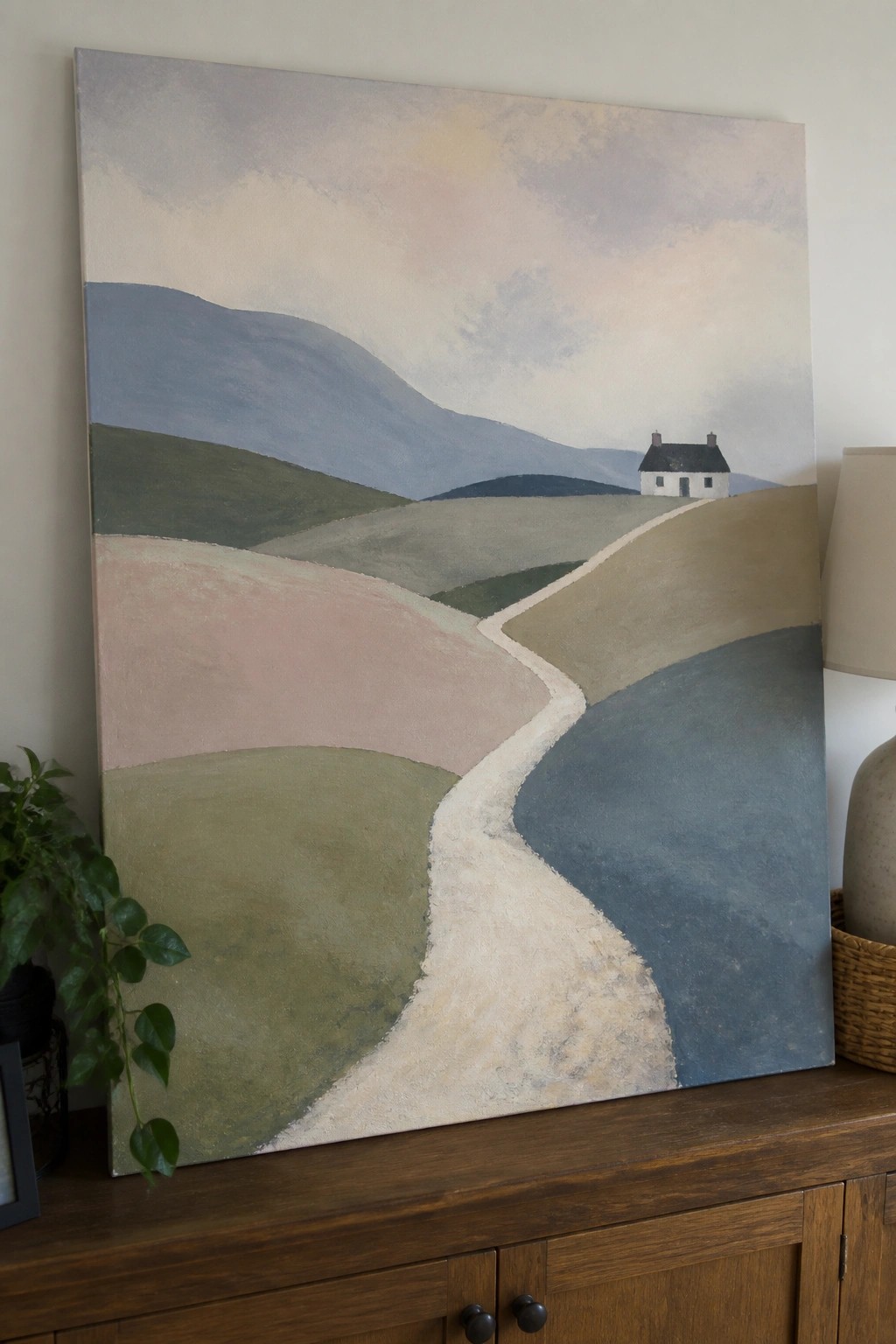Abstract painting of rolling hills in soft hues with winding path to white cottage.