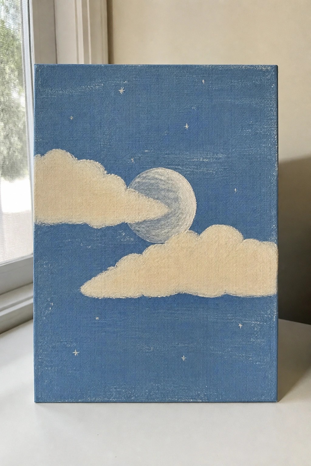Canvas painting of starry blue night sky with clouds and moon.
