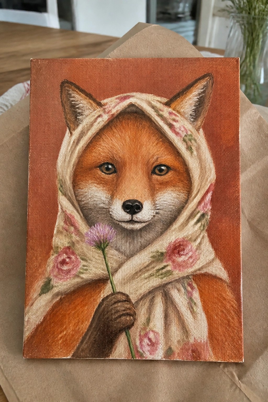 A realistic oil painting of a fox wearing a cream floral headscarf and holding a purple flower against an orange background.