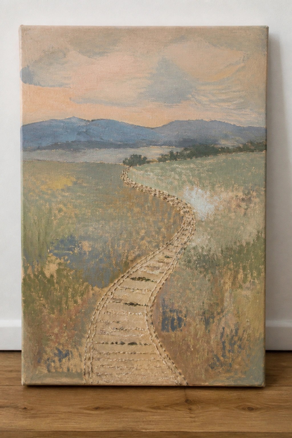 Landscape painting with stitched winding path through fields toward blue hills at dusk.