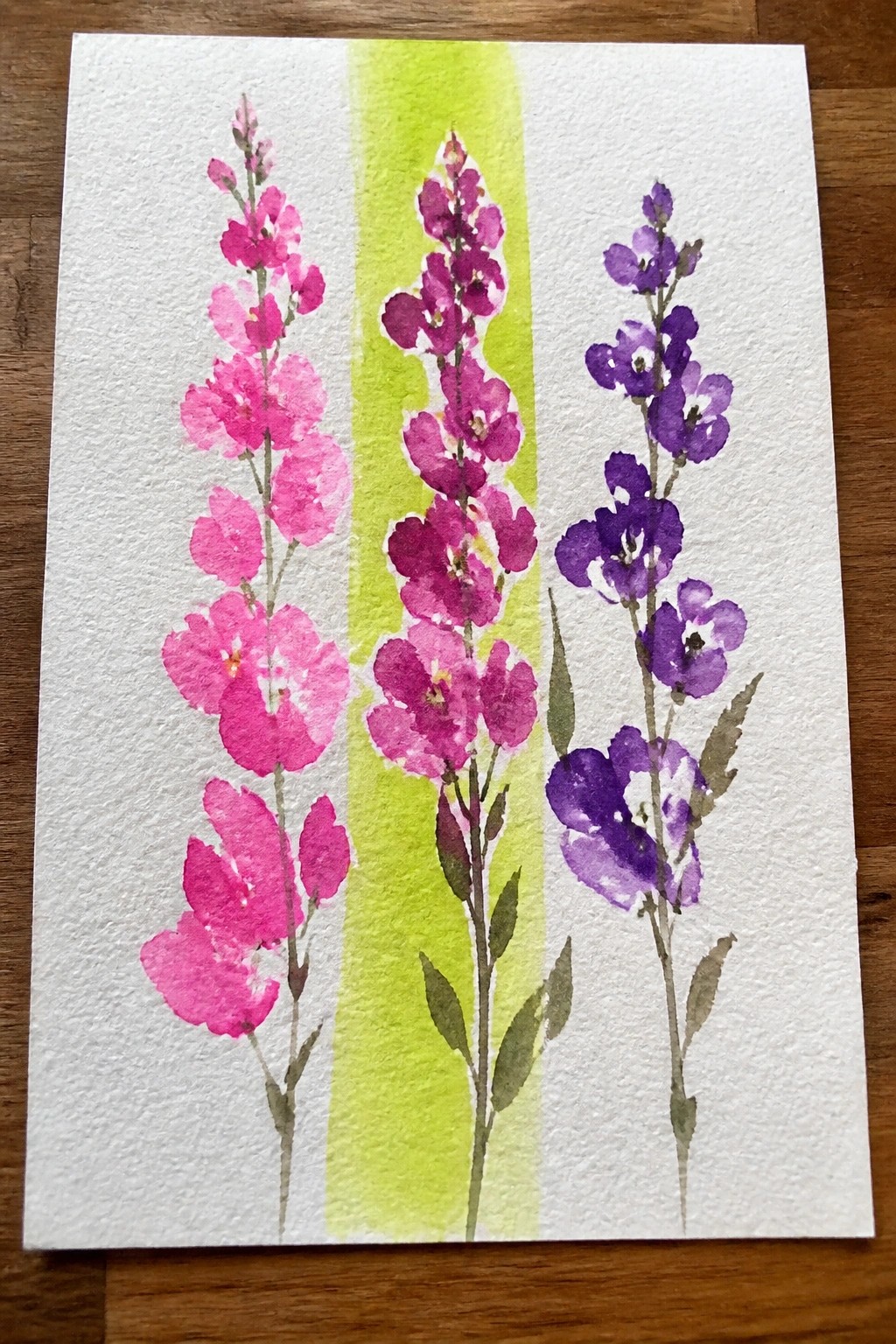 Three pink-to-purple watercolor flower stalks with green stems on lime wash